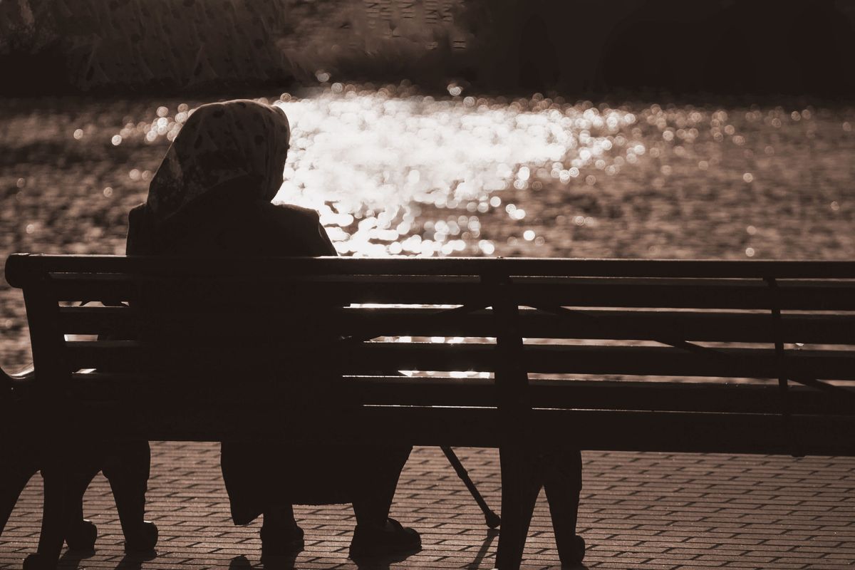 Silhouette,Of,An,Elderly,Woman,Holding,Cane,Sitting,On,Bench.