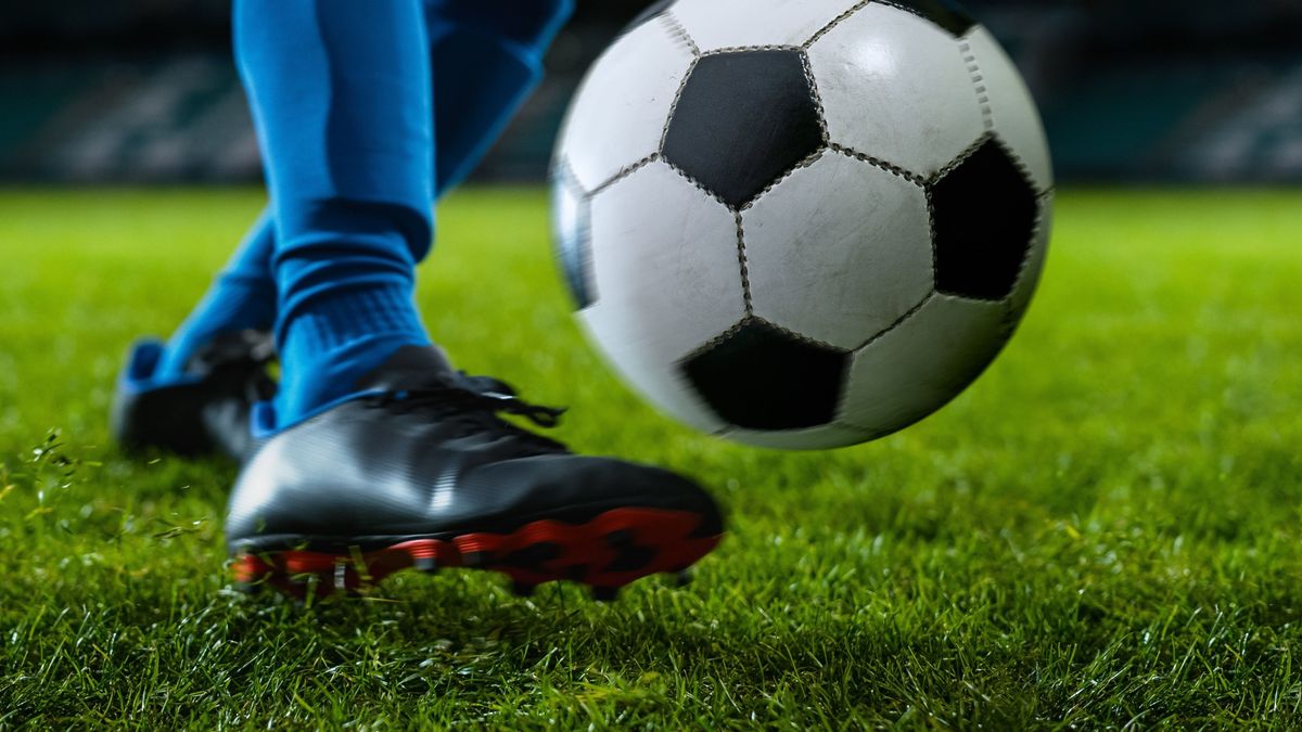 Close-up,Of,A,Leg,In,A,Boot,Kicking,Football,Ball.