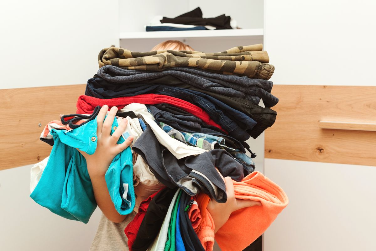 Boy,Holding,A,Huge,Pile,Of,Clothes.,Kid,Makes,Order