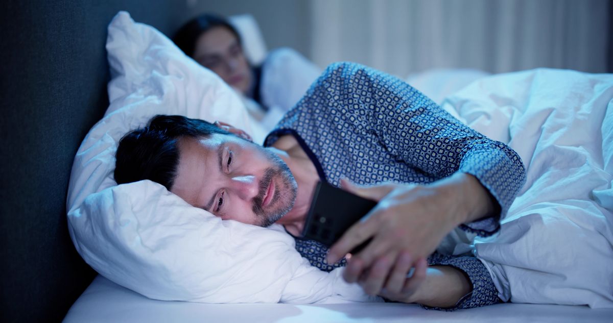 Young,Man,Using,Cellphone,While,Her,Wife,Sitting,On,Bed